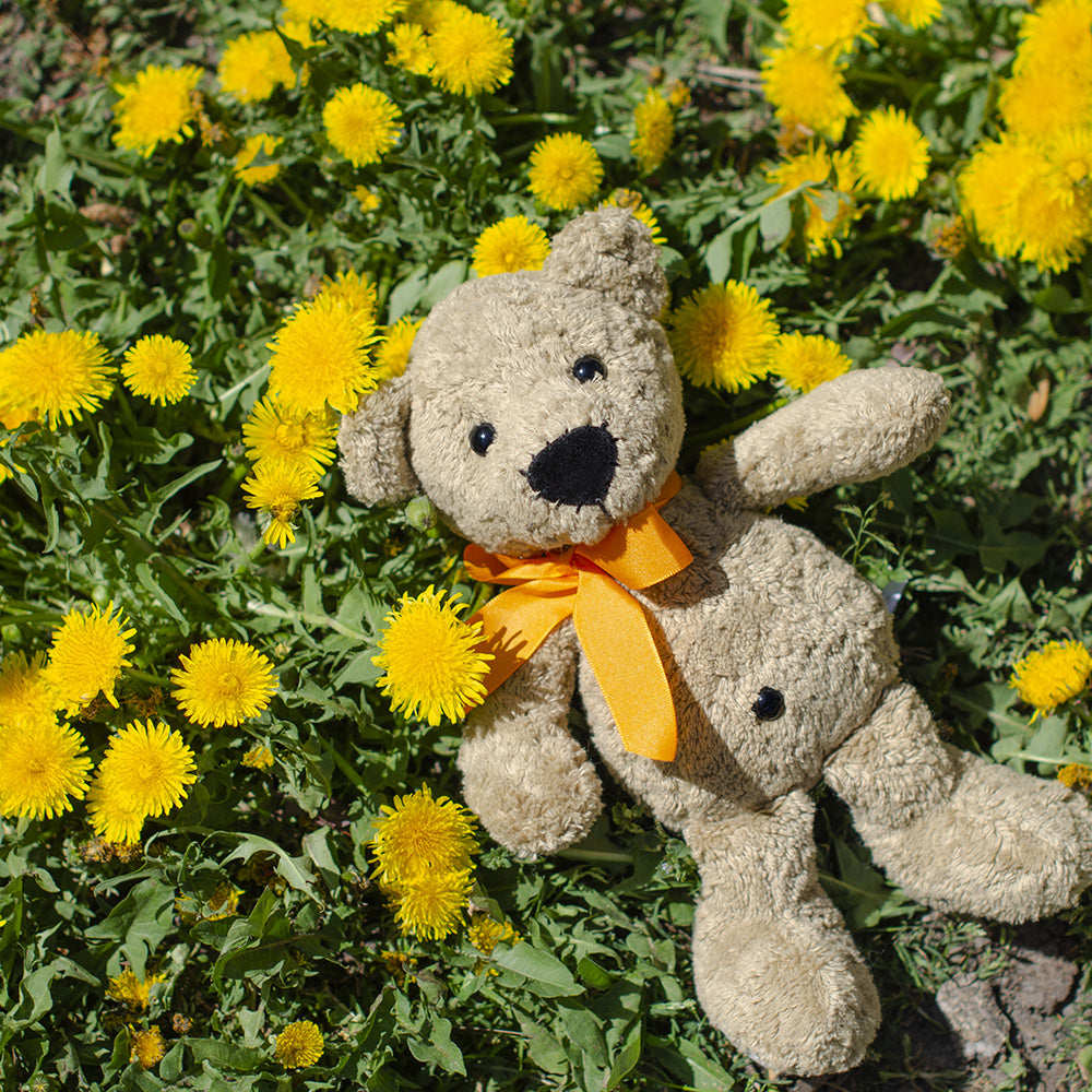 Steiner Bio Teddybär Bruno in braun mit schwarzen Augen & orangem Halsband auf der Löwenzahnwiese