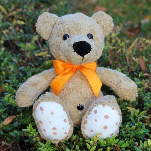 Steiner Bio Teddybär Bruno in braun mit schwarzen Augen & orangem Halsband auf der Wiese