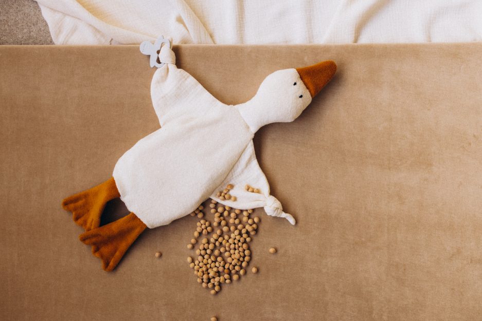 Weiches Wärmekissen mit Kirschkernfüllung in Form einer Gans aus Bio-Baumwolle mit senfgelben Füßen und Schnabel sowie integriertem Beißring für Babys.